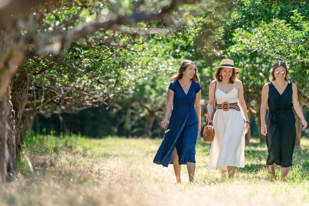 three young women walking in a sunny orchard