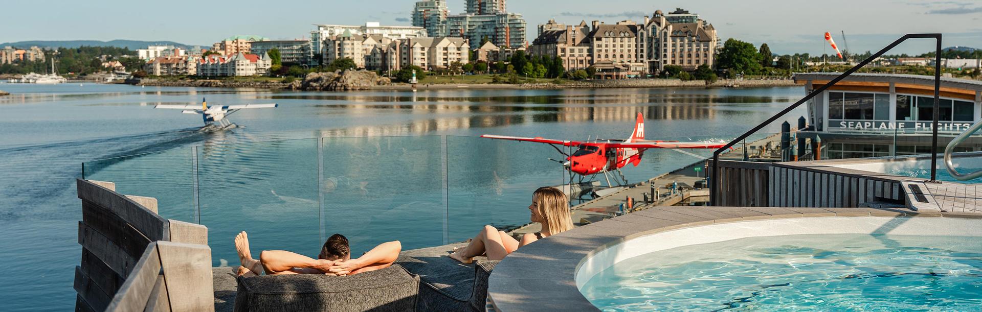 A couple lounges on the deck at HAVN Saunas watching seaplanes taxi on the Inner Harbour in Victoria, BC