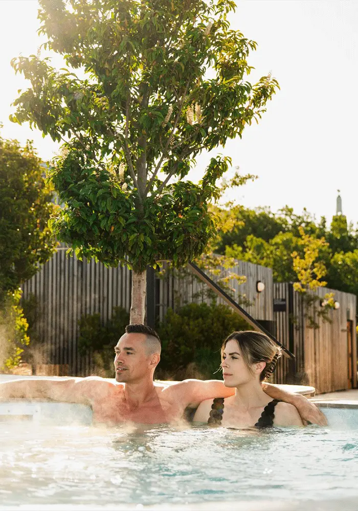 A couple soaks in a hot tub beneath the trees on the deck of HAVN Saunas, a floating sauna experience on Victoria, BC's Inner Harbour