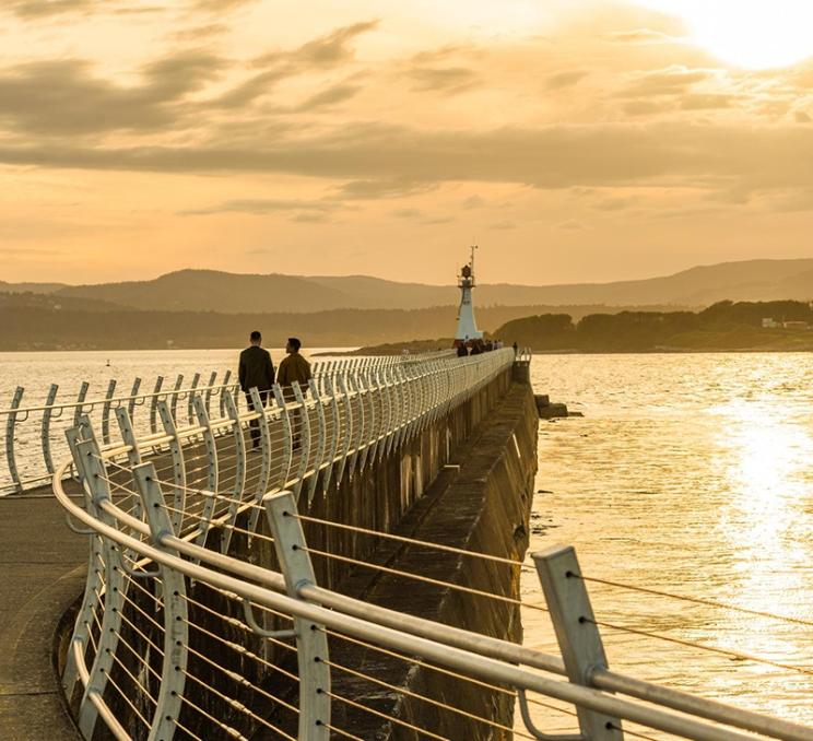 A couple walks along the Ogden Point Breakwater at sunset in Victoria, BC