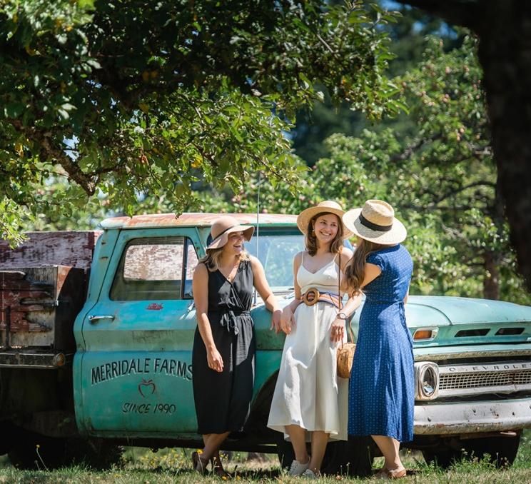 Three women chat next to a truck in the orchard at Merridale Cidery & Distillery