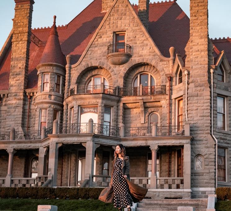 A woman stands outside Craigdarroch Castle at sunset in Victoria, BC