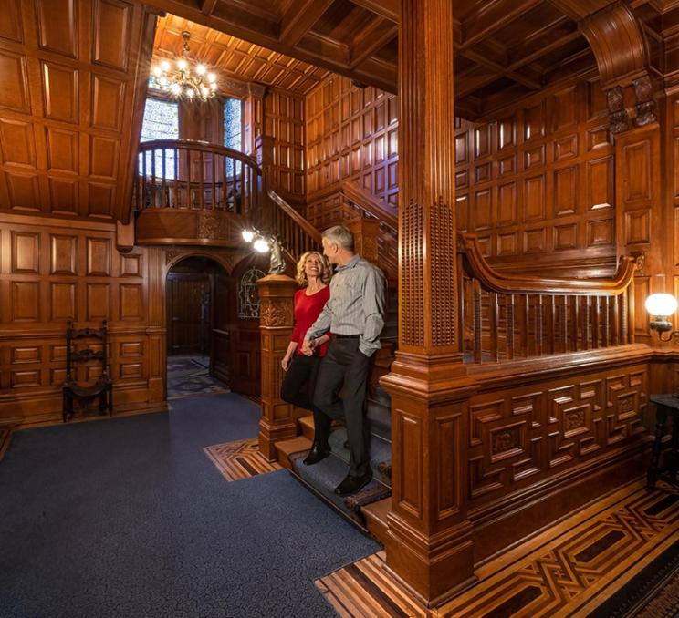 A couple walks down a staircase at Craigdarroch Castle in Victoria, BC