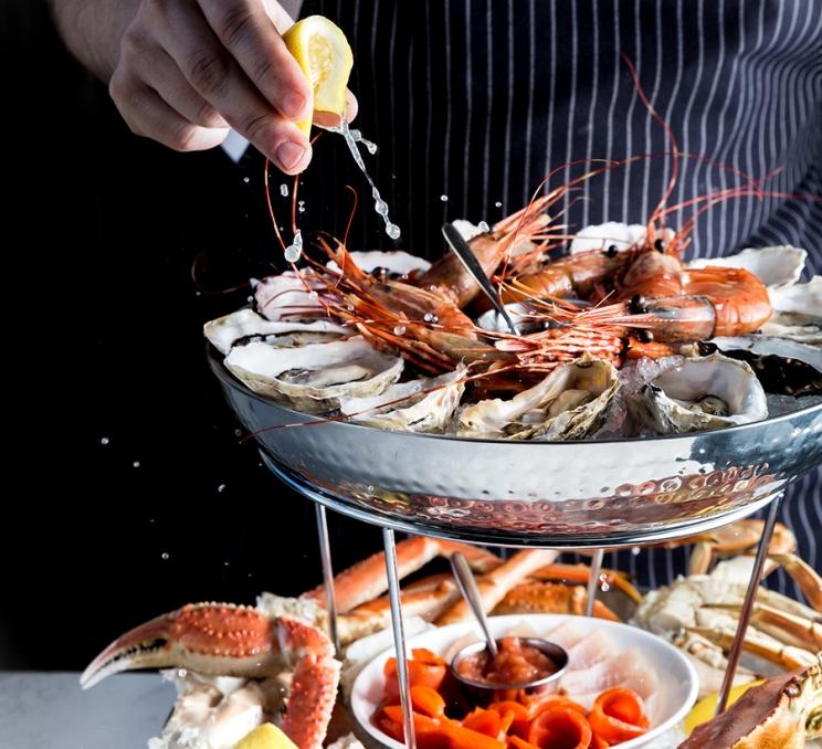 A server squeezes fresh lemon onto a seafood tower at The Courtney Room in Victoria, BC