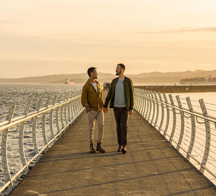 A couple walks hand-in-hand along the Ogden Point Breakwater in Victoria, BC