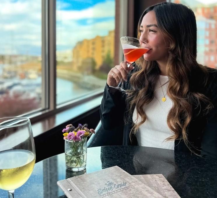 A woman enjoys a cocktail and an ocean view at Blue Crab Seafood House in Victoria, BC