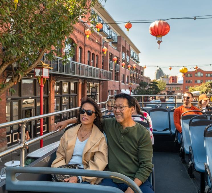 A couple rides through Victoria's historic Chinatown aboard a hop-on hop-off bus tour.