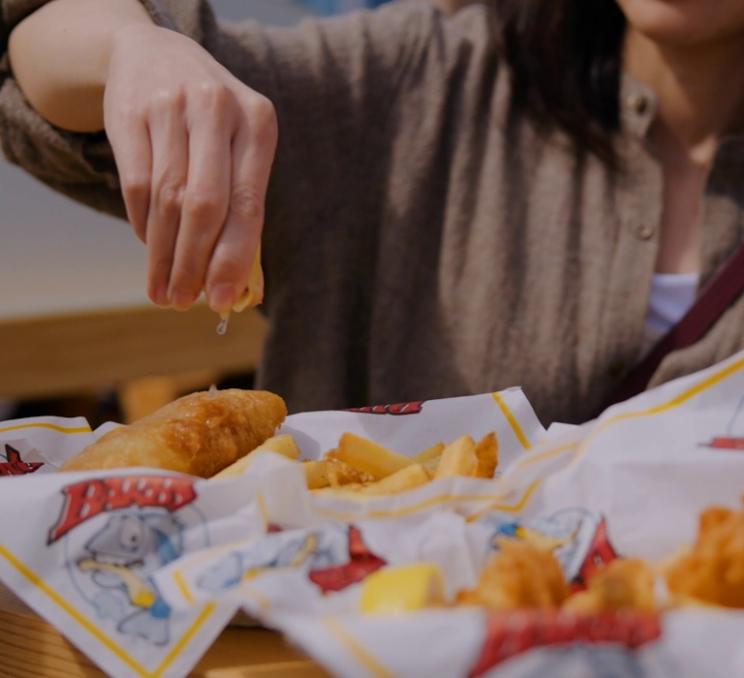 A woman squeezes a lemon overtop Barb's Fish & Chips in Victoria, BC