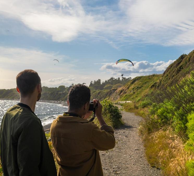 A couple photographs paragliders along Dallas Road in Victoria, BC