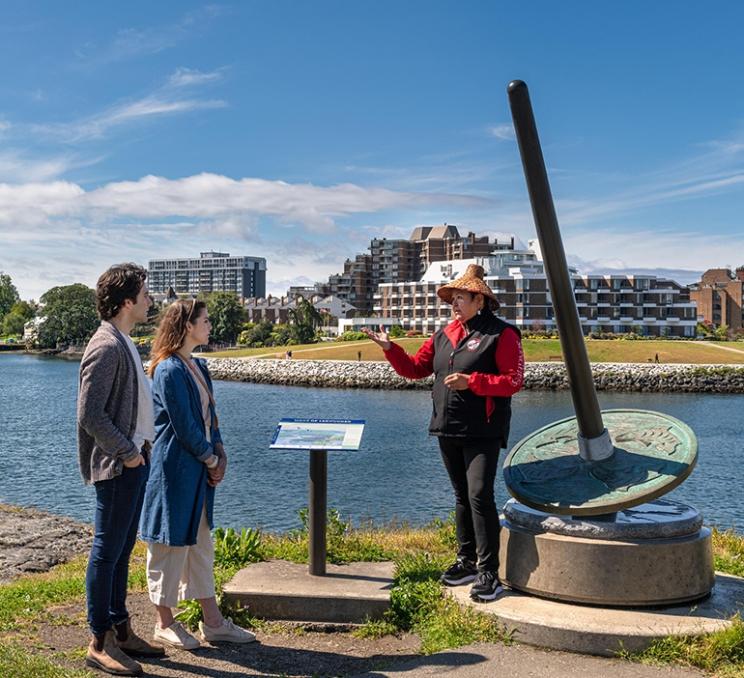 A guide shows visitors a Seven Signs of the Lekwungen sculpture in Victoria, BC