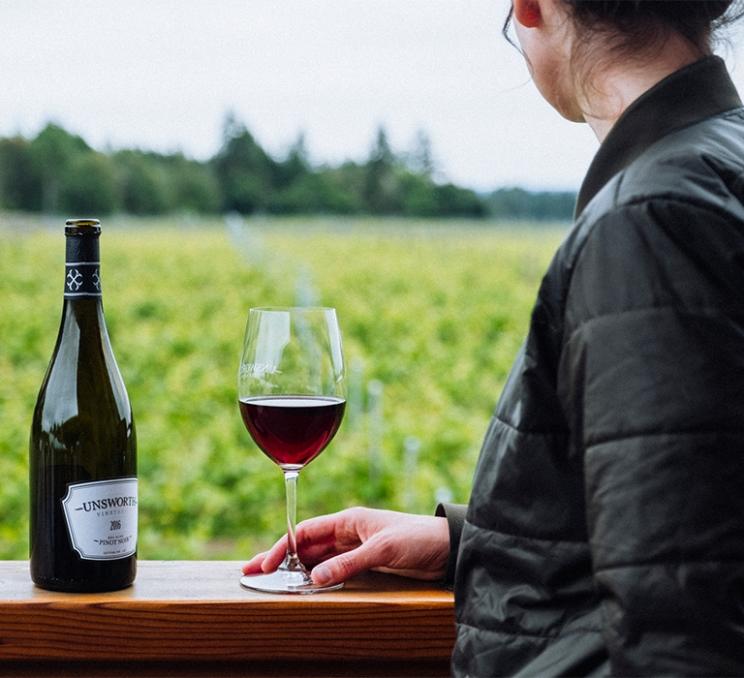 A woman enjoys a glass of red wine at the side of the vineyard at Unsworth Vineyards in Victoria, BC