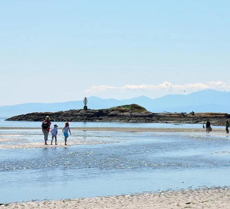 A family walks across the beach at Witty's Lagoon Regional Park in Victoria, BC