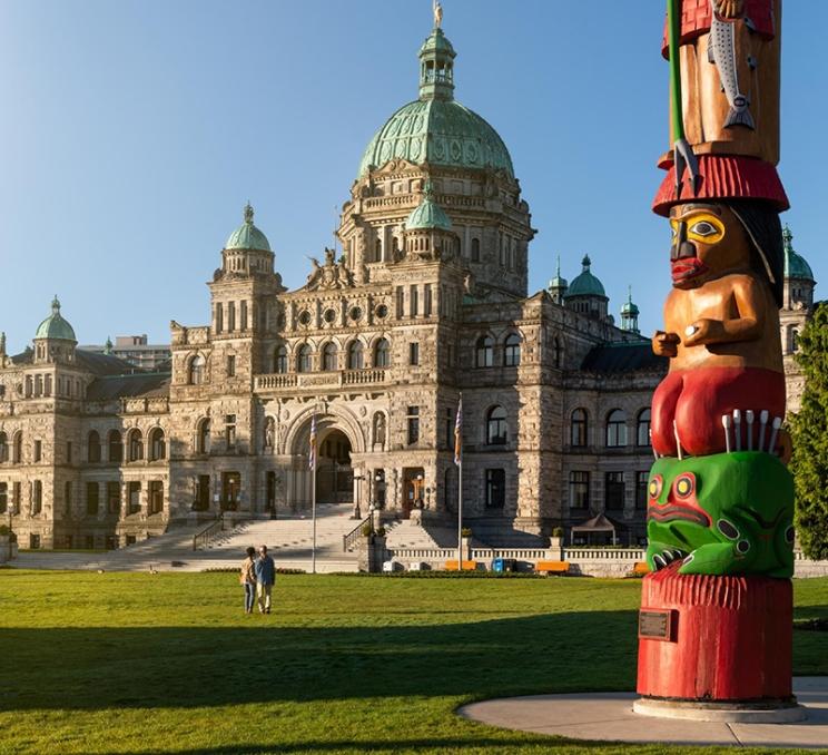 A couple walks across the lawn of the BC Parliament Buildings in Victoria, BC