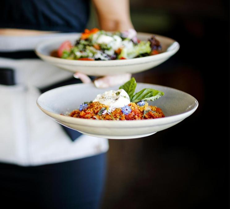 A server carries two plates of food at Boom + Batten in Victoria, BC