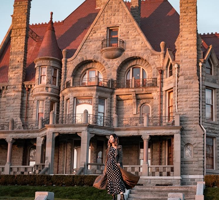 A woman in a dress stands outside Craigdarroch Castle in Victoria, BC