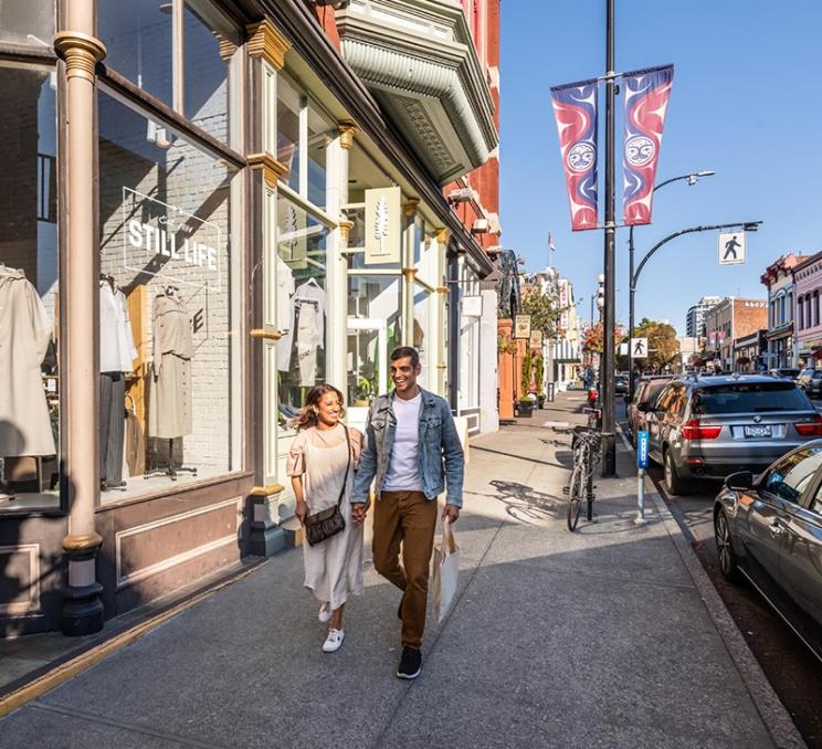 A couple walks along the shops on Johnson Street in Victoria, BC