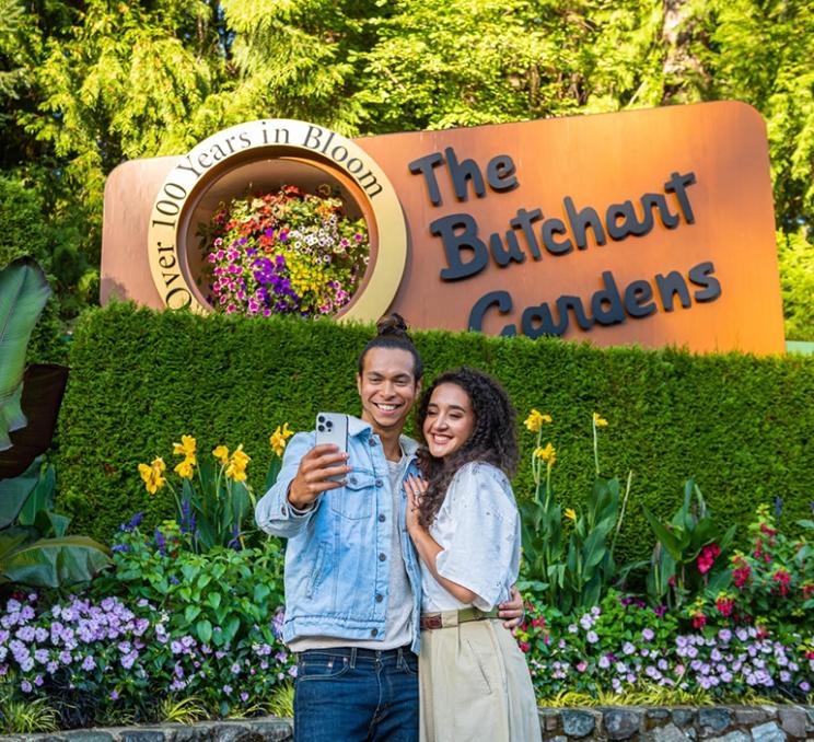 A couple takes a selfie in front of a sign at The Butchart Gardens in Victoria, BC