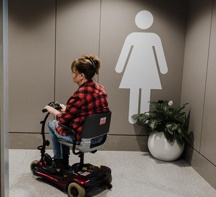 A person with a disability uses a mobility scooter to enter an accessible washroom at YYJ - Victoria International Airport in Victoria, BC