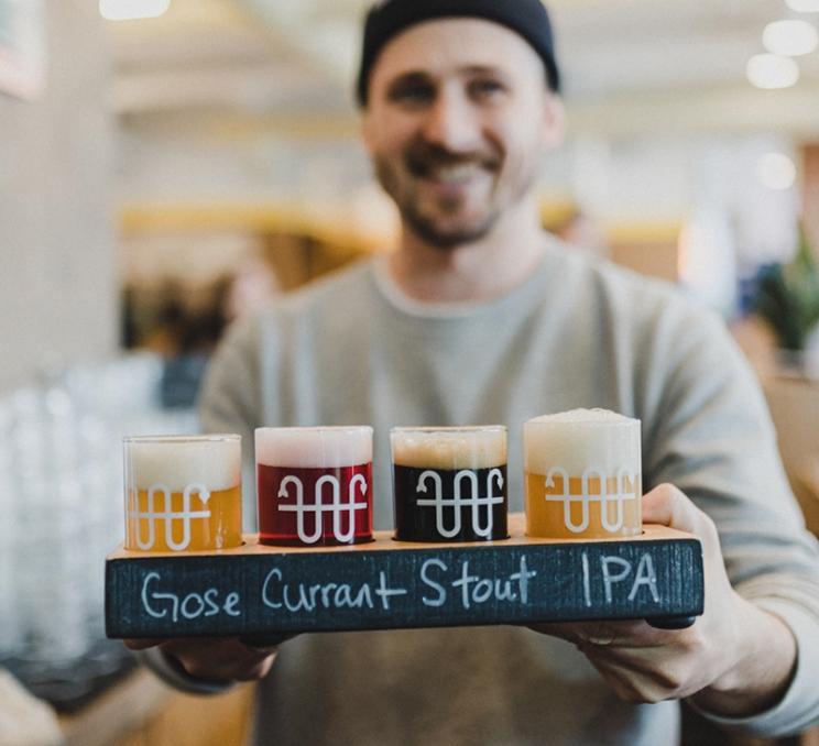 A server brings a flight of beers to a table at Whistle Buoy Brewing in Victoria, BC