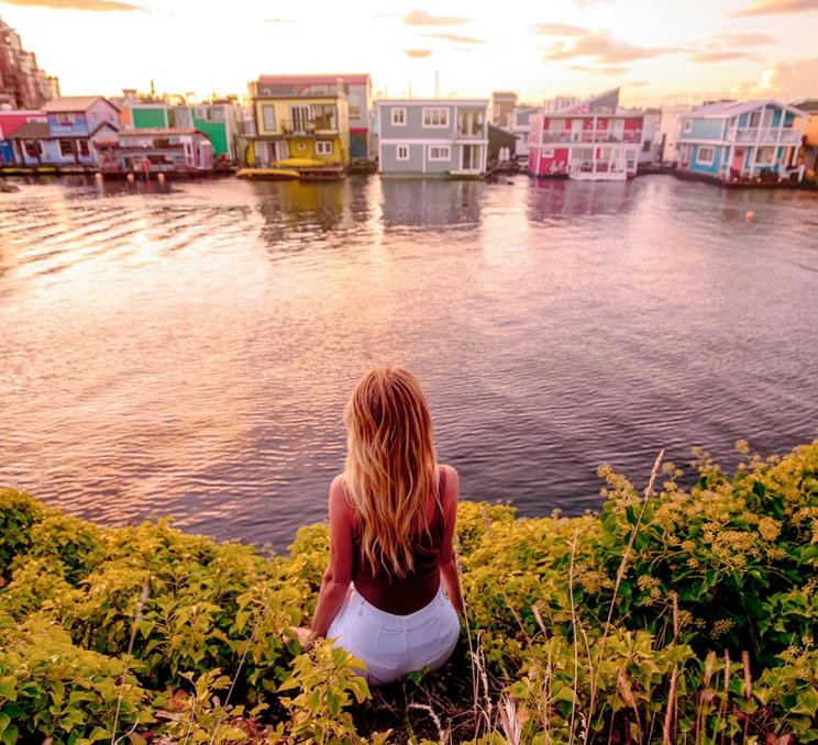 A woman sits along the shoreline across from Fisherman's Wharf in Victoria, BC