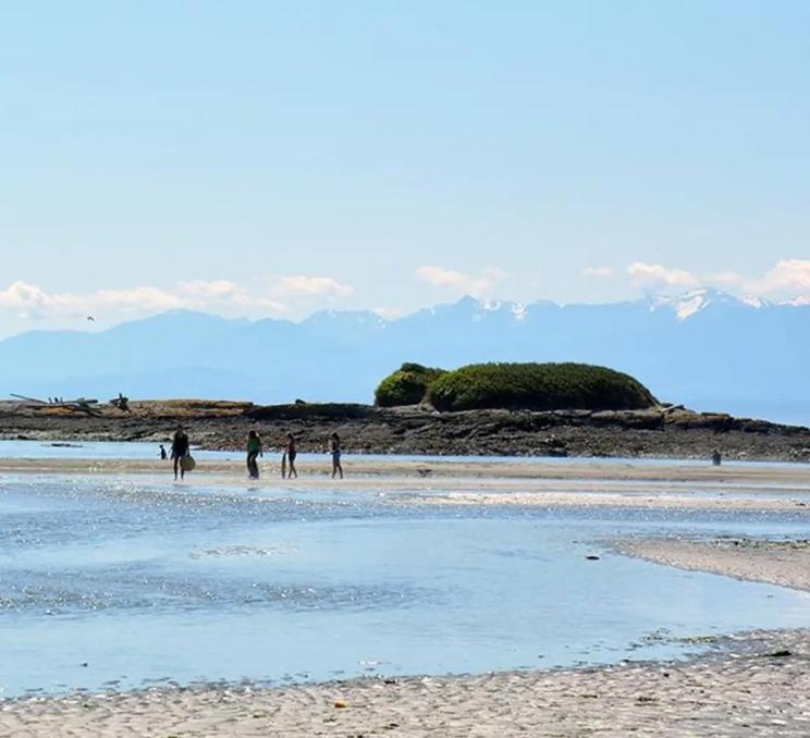 People walk across the beach at Witty's Lagoon Regional Park in Victoria, BC