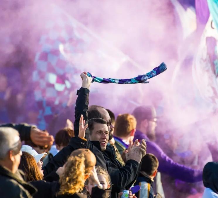 A group of fans cheer, one waving a scarf, at a Pacific Football Club in Victoria, BC