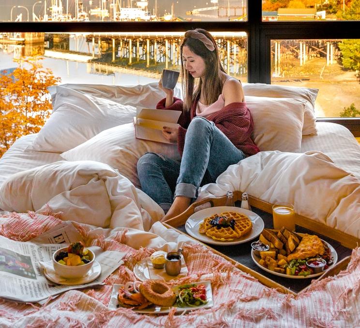 A woman enjoys a large spread of breakfast in bed at a Victoria, BC hotel