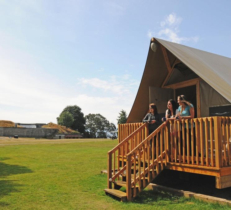 A group of friends stand on the porch of an oTENTiks tent at Fort Rodd Hill & Fisgard Lighthouse National Historic Site in Victoria, BC