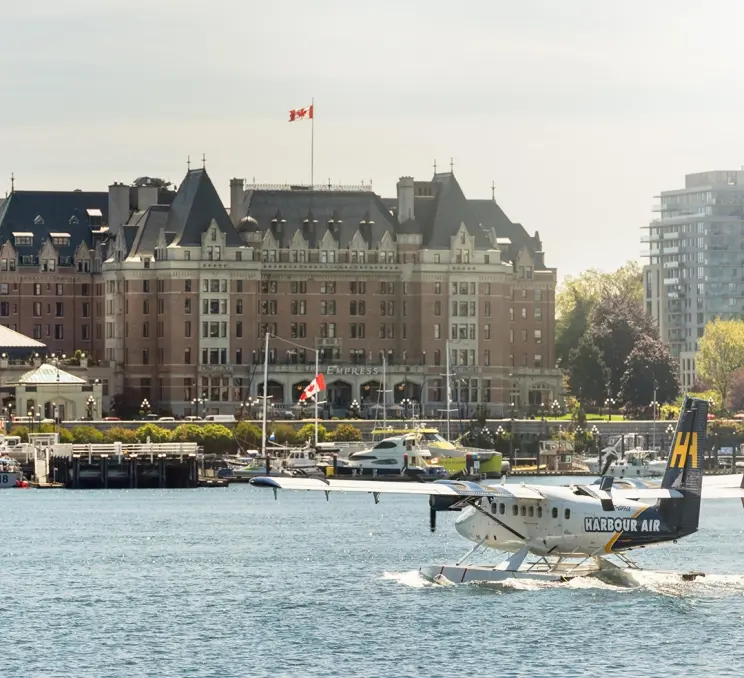A Harbour Air Seaplanes flight lands on the water on the Inner Harbour with the Fairmont Empress Hotel in the background in Victoria, BC